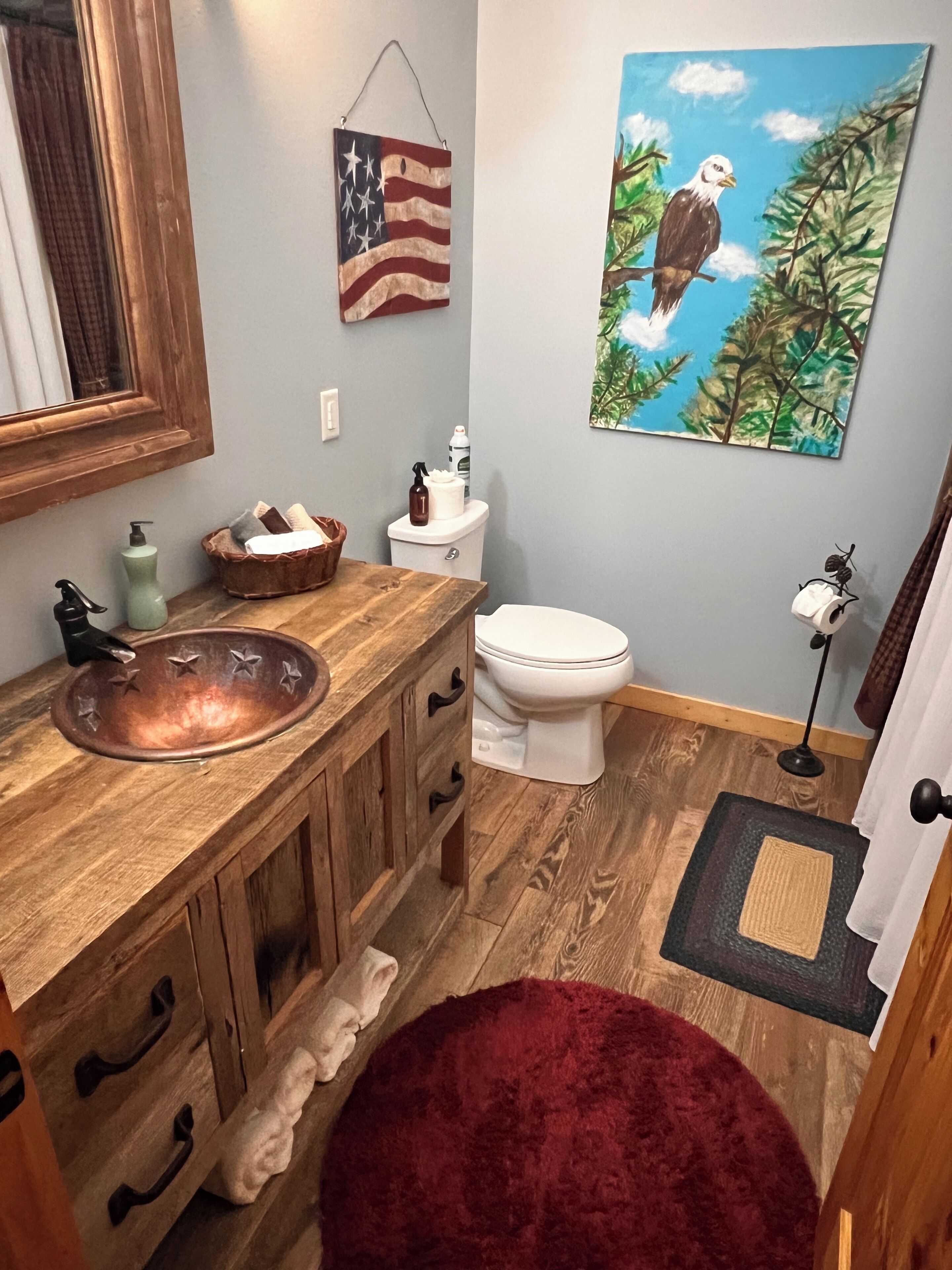 Ein Badezimmer mit einem Holzbadezimmermöbel, einem Kupferspülbecken, einer Toilette und einem Gemälde eines Adlers.