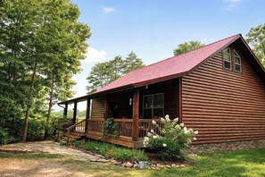 A log cabin with a porch, surrounded by trees and a stone pathway.