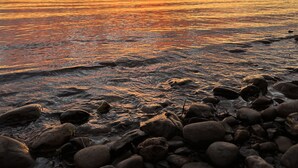 Un coucher de soleil sur une côte rocheuse, avec une eau calme qui reflète les couleurs du ciel.