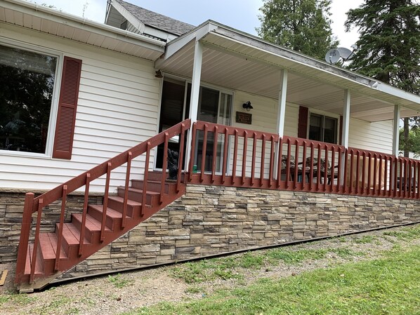 A two-story house with a stone foundation and a red staircase leading to a covered porch. - Cozy Cottage on Long Lake in Beautiful Northern Aroostook County, Maine (St. David)