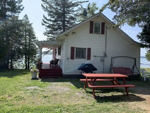 A small cabin with a porch, a picnic table, and a swing set. - Cozy Cottage on Long Lake in Beautiful Northern Aroostook County, Maine (St. David)