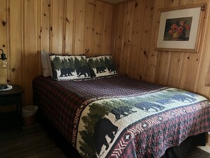 A wooden-paneled room with a bed, a nightstand, a lamp, and a framed picture on the wall. - Cozy Cottage on Long Lake in Beautiful Northern Aroostook County, Maine (St. David)
