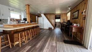 Une cuisine avec un bar en bois et des tabourets, un réfrigérateur et un escalier menant à une autre pièce.