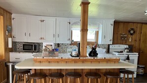 Une cuisine dotée d’un îlot central, de tabourets en bois, de meubles blancs, d’un four à micro-ondes, d’une cuisinière et d’une poubelle.
