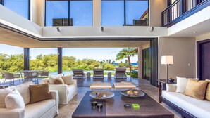 A spacious living area with a high ceiling, large windows, and a view of the outdoors.