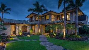 A two-story house with a stone pathway leading to the entrance, surrounded by well-maintained grass and palm trees.