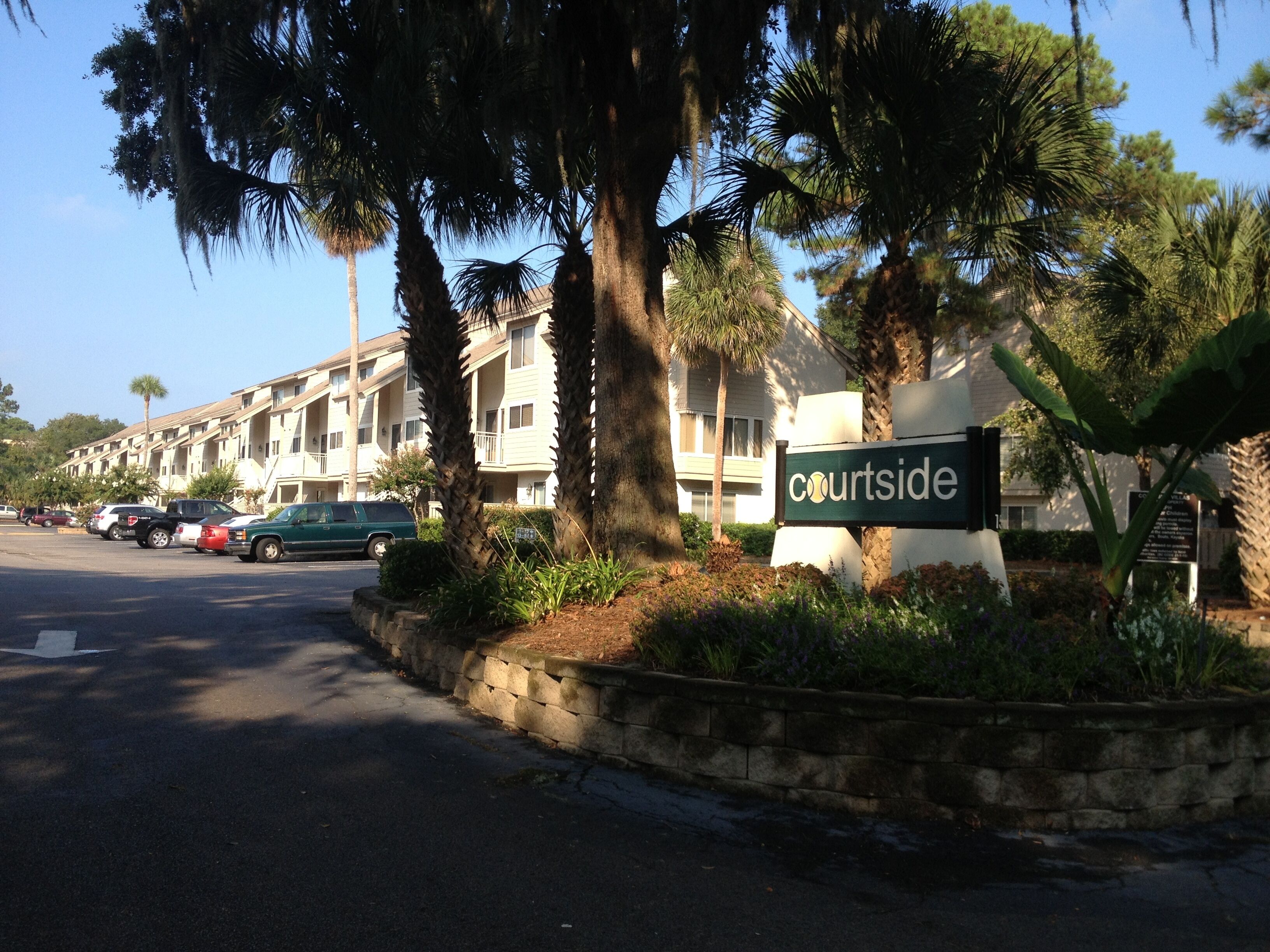 A Courtside hotel with a sign, parked cars, and palm trees.