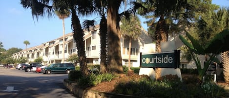 A Courtside hotel with a sign, parked cars, and palm trees.