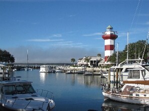 Uma marina com barcos atracados, um farol e uma ponte ao fundo.