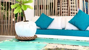 A modern outdoor seating area with a white sofa and blue cushions, a decorative plant in a white pot, and a mosaic-tiled floor.