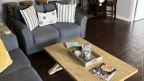 Sala de estar com sofá cinza, mesa de centro de madeira e canto de jantar com mesa e cadeiras de madeira.