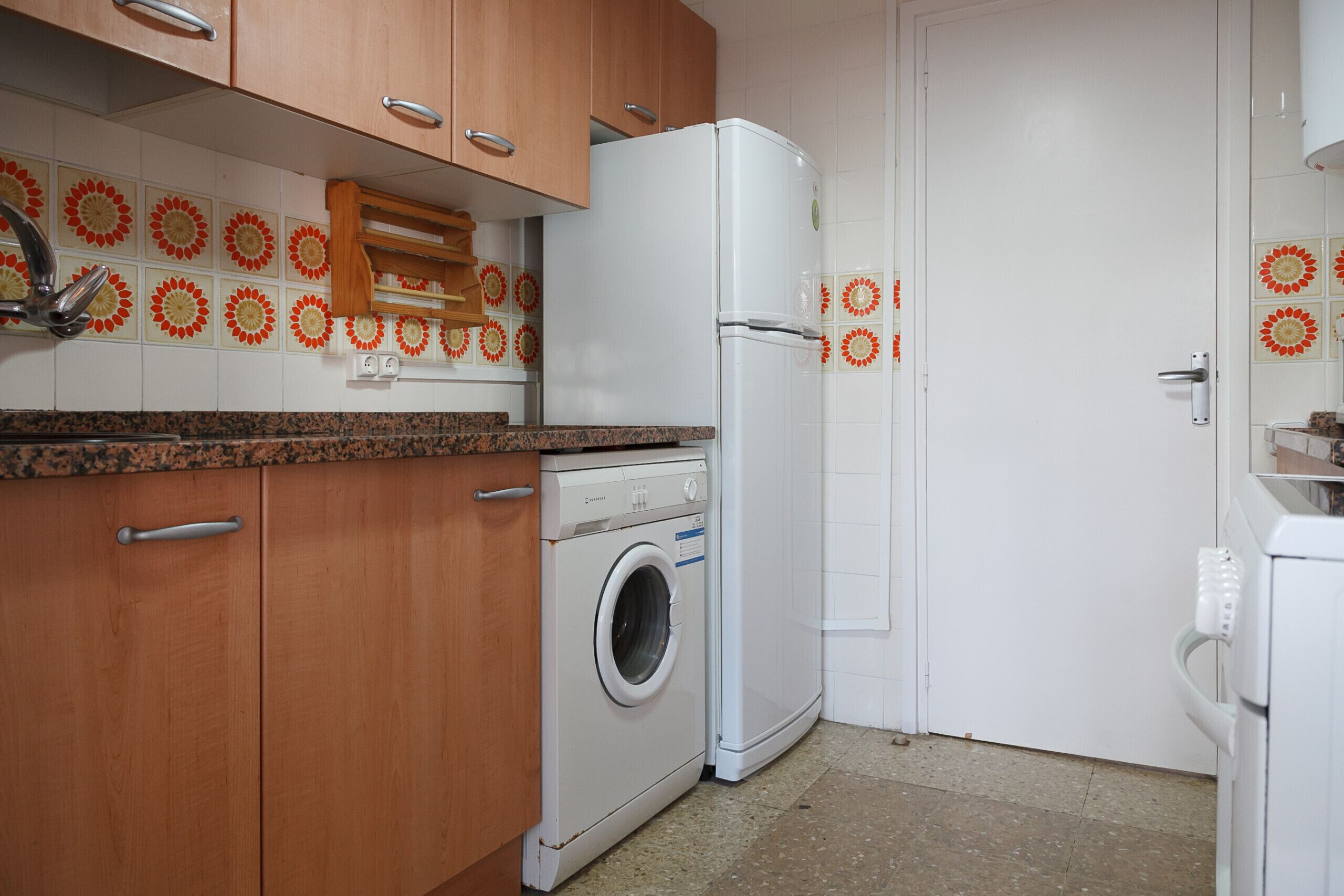 A kitchen with wooden cabinets, a washing machine, a refrigerator, and decorative tiles on the wall.