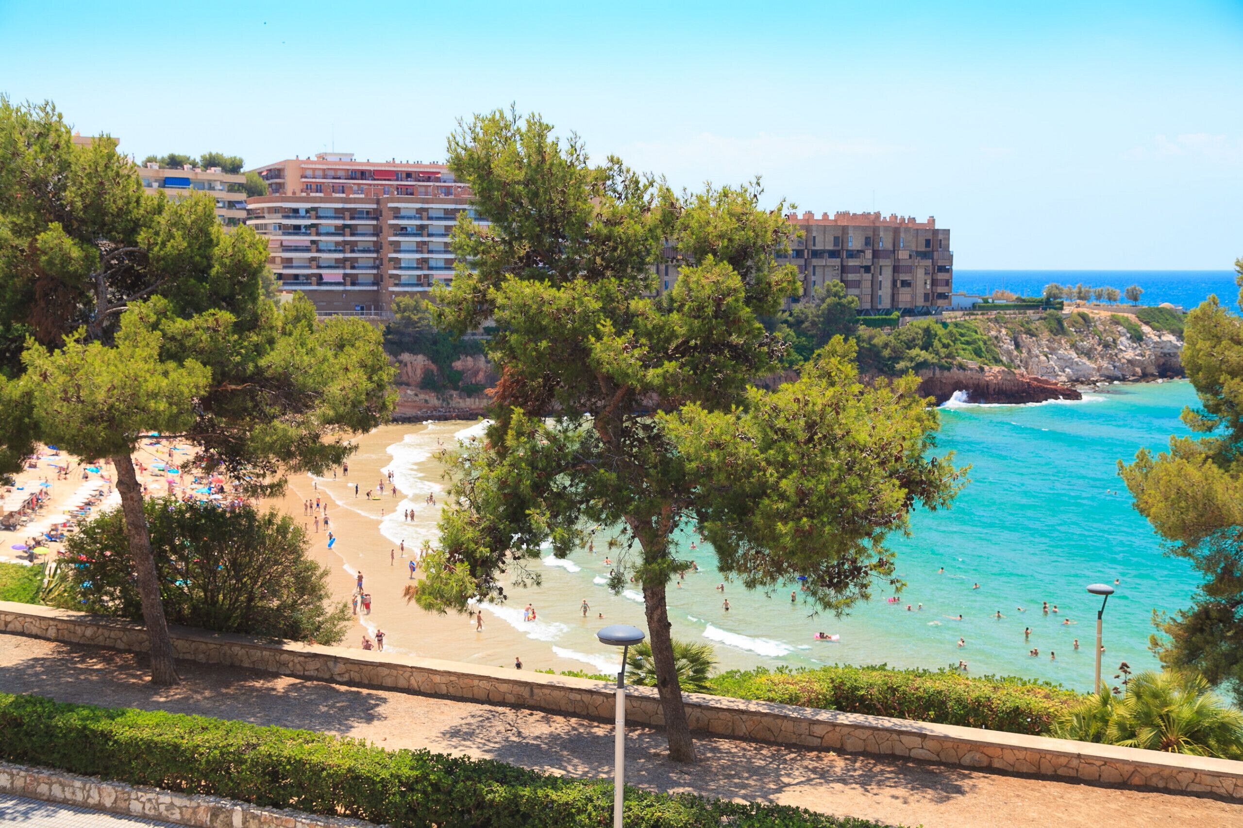 Una playa con gente, un muro de piedra y un edificio al fondo.