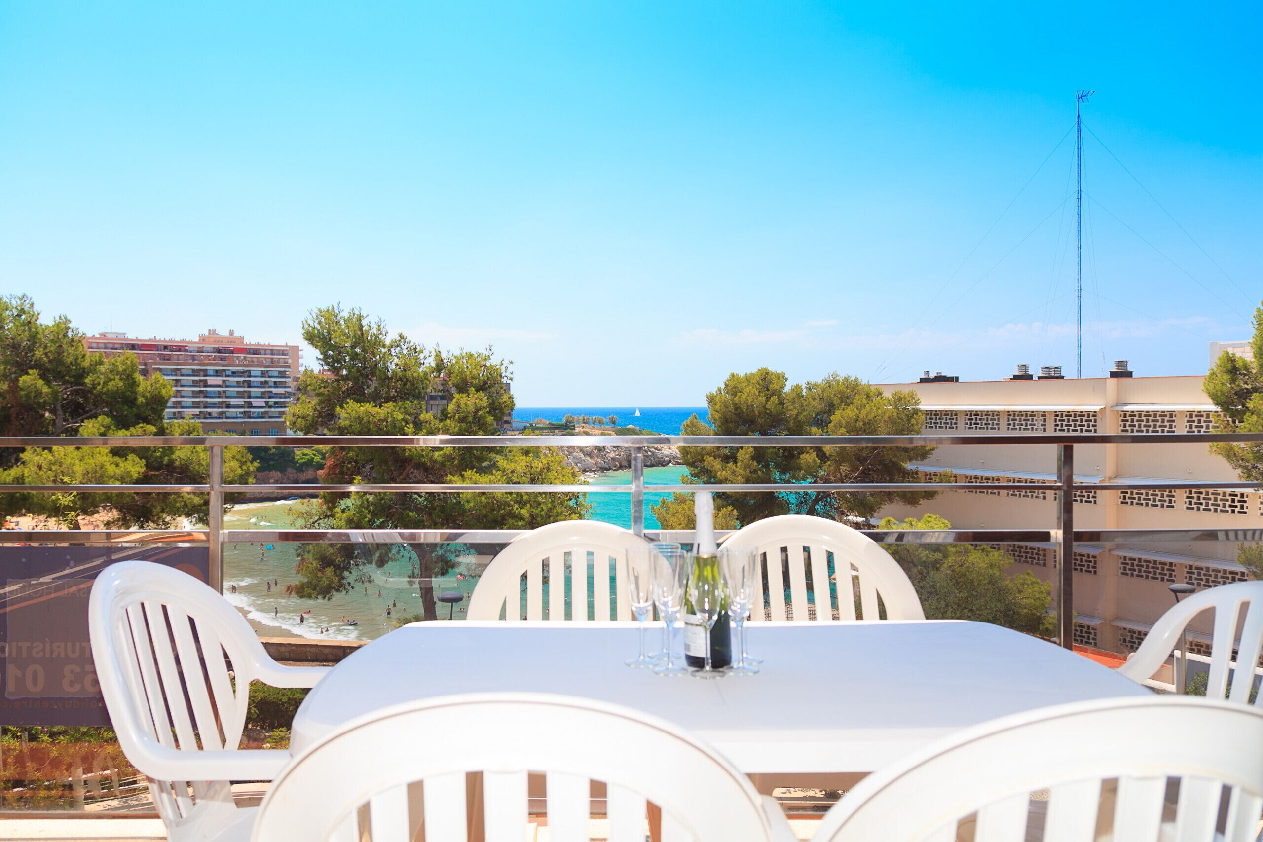 Une terrasse avec une table et des chaises donnant sur une plage et sur le paysage urbain.