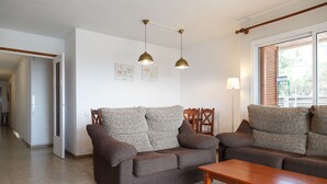 A living room with a brown sofa, a wooden coffee table, and two pendant lights. There is a door leading to another room and a window with blinds. - Spacious apartment with sea views and pool - UHC MARINA MAR (Salou)