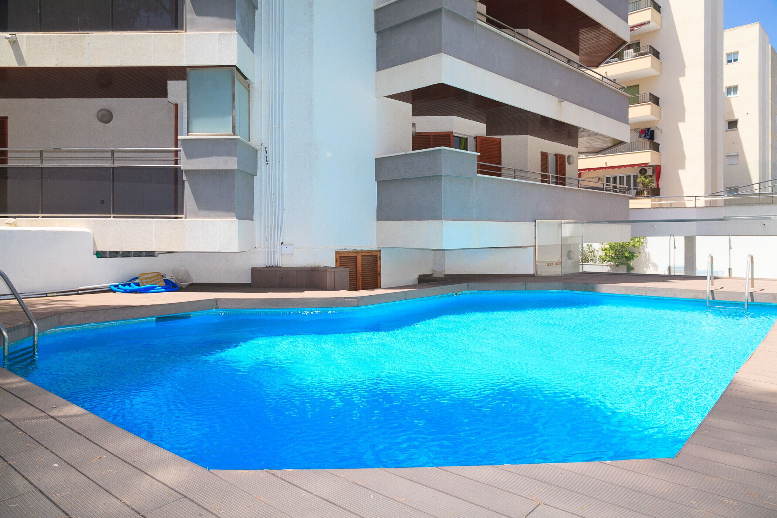 Una piscina con cubierta de madera, rodeada por un edificio de varios pisos con balcones.