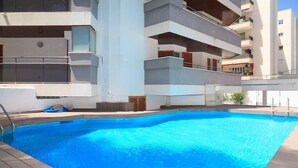 A swimming pool with a wooden deck, surrounded by a multi-story building with balconies. - Spacious apartment with sea views and pool - UHC MARINA MAR (Salou)