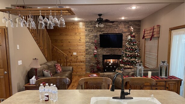 A cozy living room with a fireplace, a Christmas tree, and a dining area with a sink and water bottles. - Convenient Prime Location, Exceptional reviews!! We would love to host you. (Pigeon Forge)
