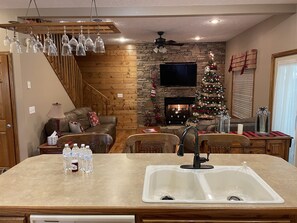 Ein gemütliches Wohnzimmer mit Kamin, Weihnachtsbaum und Essbereich mit Spüle und Wasserflaschen.