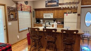 A kitchen with wooden cabinets, a microwave, a refrigerator, and a bar area with stools. - Convenient Prime Location, Exceptional reviews!! We would love to host you. (Pigeon Forge)