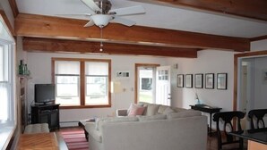 A spacious living area with a sofa, wooden floor, ceiling fan, and large windows. - Amazing Falmouth Heights House Just Steps Away from Beach (Falmouth)