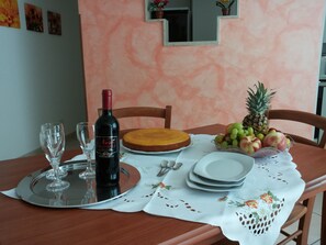 A dining table set with a cake, a bottle of wine, and a fruit bowl.