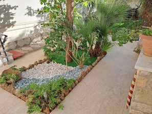 A garden area with a variety of plants, a small water feature, and a seating area with a red mat.