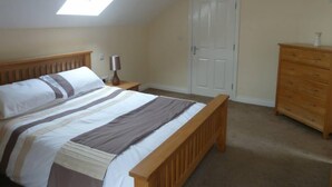 Ein Schlafzimmer mit Bett, Schminktisch, Nachttisch, Lampe, Tür und Dachfenster.