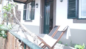Una valla de madera con una rama, un edificio blanco con contraventanas verdes y dos sillones de descanso.