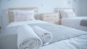 Una cama bien hecha con toallas blancas enrolladas, un cabecero de madera y una mesita de noche con una lámpara.