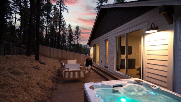 Een hottub buiten een huis met een houten terras en stoelen, omringd door een hek en bomen.