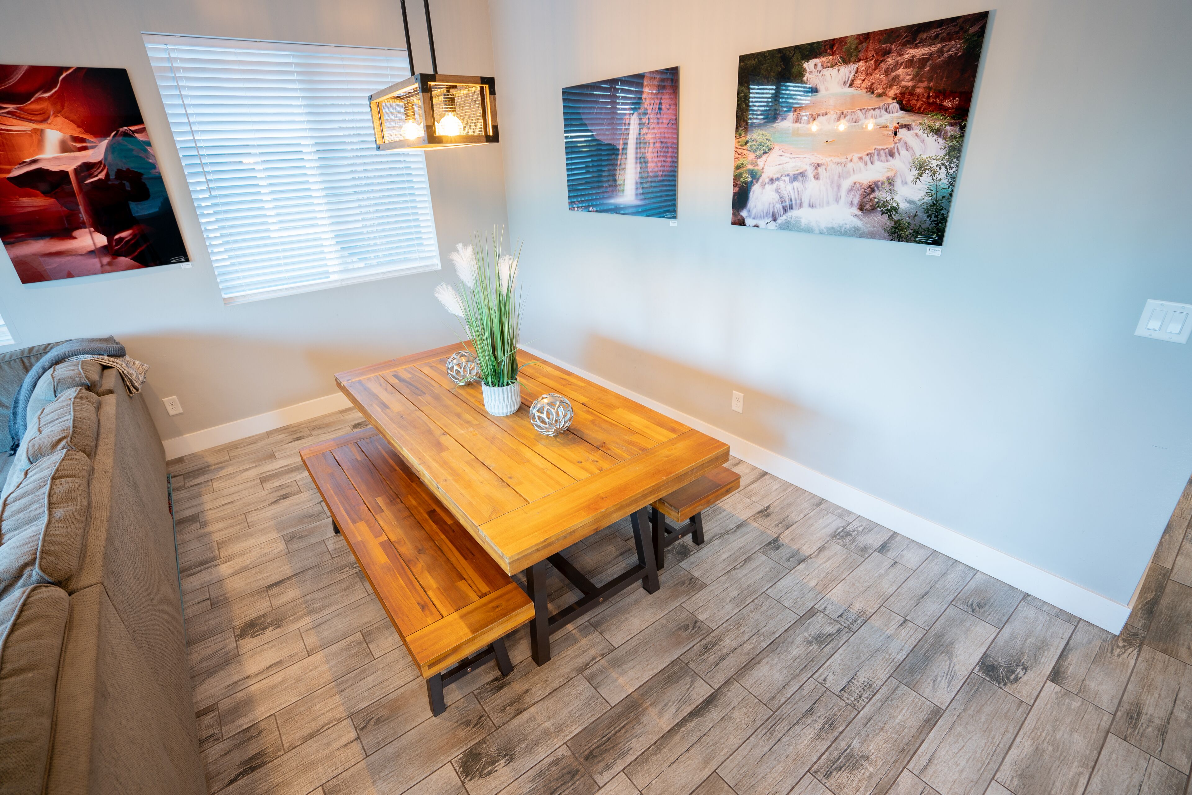 A dining area with a wooden table and benches, a sofa, and three framed pictures on the wall.