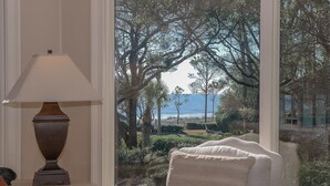 A chair facing a large window with a view of trees and the ocean.