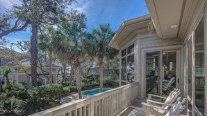 A balcony with a pool, surrounded by palm trees and other greenery.