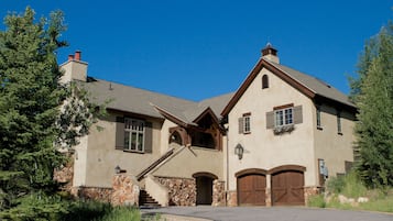 A large, two-story house with a stone foundation, a prominent staircase, and a garage with two doors.