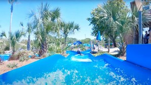 Un tobogán de agua que desemboca en una piscina azul cristalina, rodeada de palmeras y un cielo soleado.
