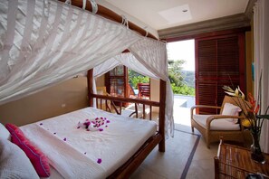 A bedroom with a canopy bed, a balcony with wicker furniture, and a view of greenery.