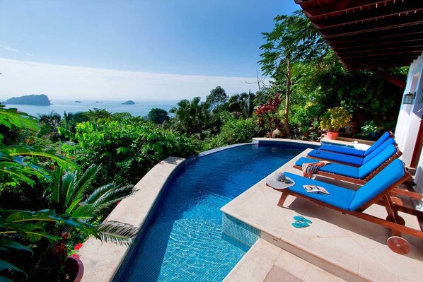 A private pool with blue lounge chairs and a view of the ocean.