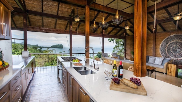 A spacious kitchen with a large island, a view of the sea, and a dining area with a sofa and decorative wall.