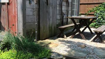 Un cobertizo de madera rústico con un letrero de 'Prohibido el paso', un banco de madera y una mesa de picnic en un jardín.