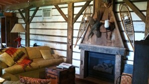 A rustic cabin interior with a wooden log wall, a sofa, a fireplace, and a woven rug.