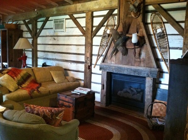 A rustic cabin interior with a wooden log wall, a sofa, a fireplace, and a woven rug.