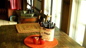 A rustic wooden table with woven placemats, a container labeled 'Farm Fresh Eggs', and a lamp.
