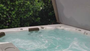 Un jacuzzi con tapa entreabierta, rodeado de exuberante follaje verde.