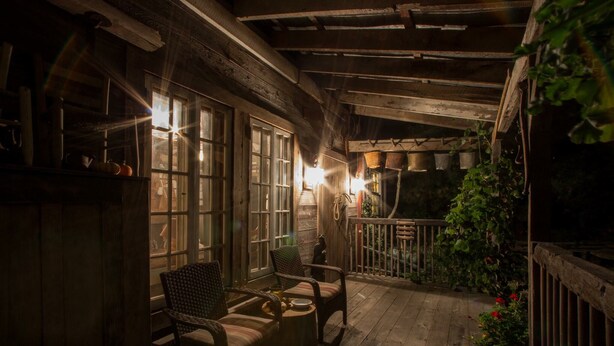 A cozy wooden porch with a seating area, a small table, and a view of the garden.