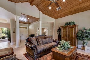 A spacious living room with a high ceiling, a large wooden cabinet, and a leather sofa. - Star Ranch Main Estate (Wimberley)