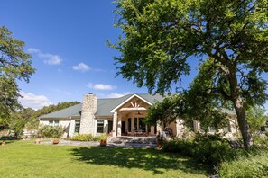 A stone house with a covered porch, a chimney, and a lawn. - Star Ranch Main Estate (Wimberley)