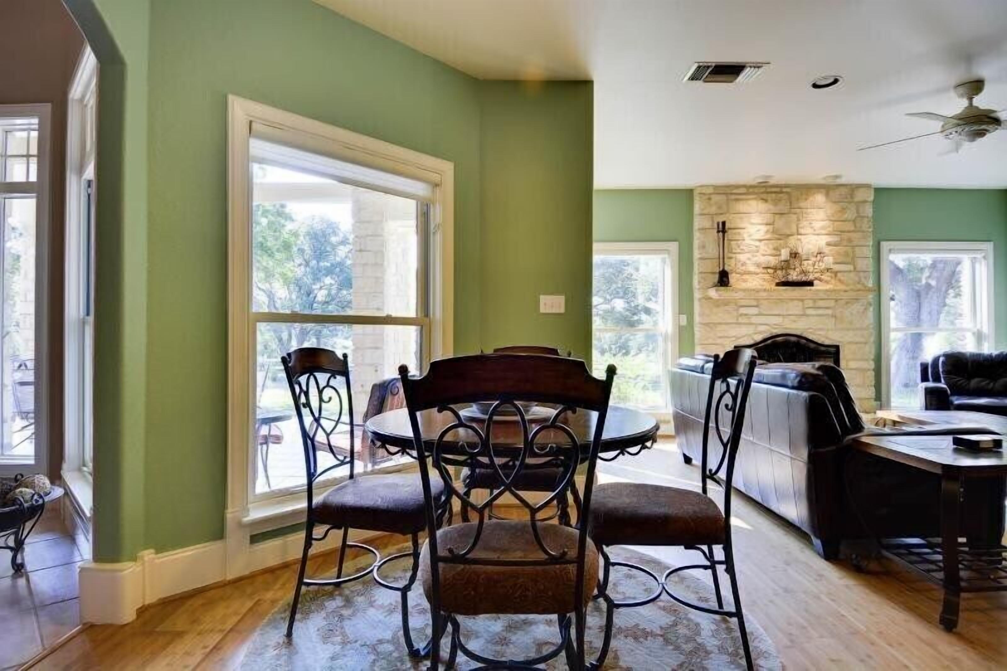 A dining area with a round table and four chairs, a stone fireplace, and a view of the outdoors through large windows.