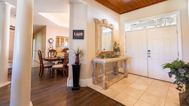 A hallway with a wooden ceiling, a white door, a console table with a mirror, and a dining area with a wooden table and chairs.