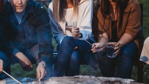 Three people sitting by a stone fire pit outdoors at dusk.